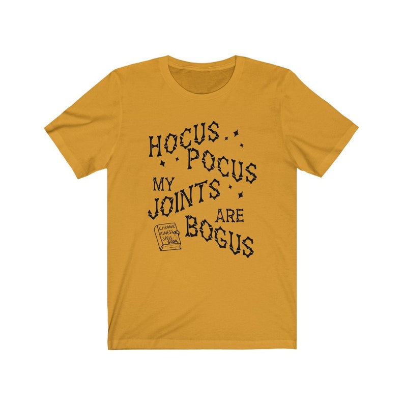 May include: A mustard yellow t-shirt with black text that reads "Hocus Pocus My Joints Are Bogus". A small black and white illustration of a book with the text "Chilling Vines Spell Book" is below the text.