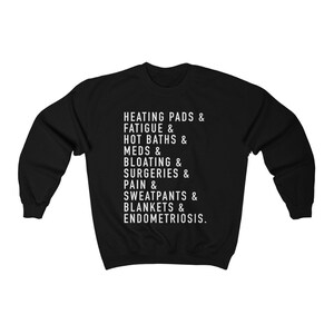May include: Black sweatshirt with white text that reads "HEATING PADS & FATIGUE & HOT BATHS & MEDS & BLOATING & SURGERIES & PAIN & SWEATPANTS & BLANKETS & ENDOMETRIOSIS."