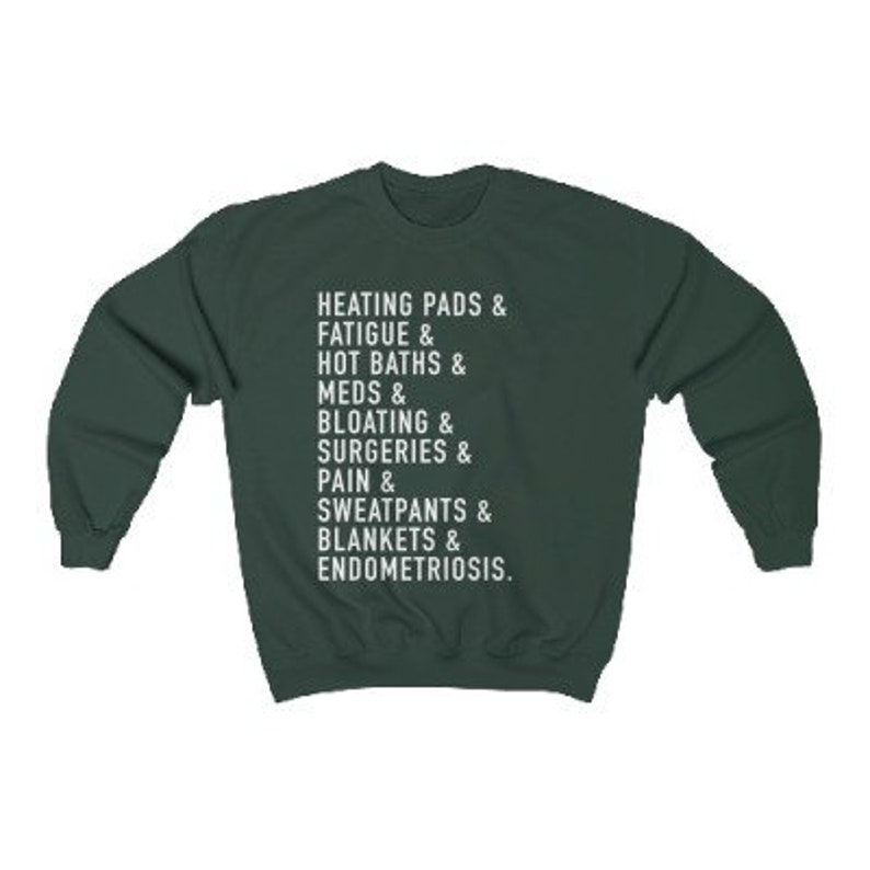 May include: A dark green sweatshirt with white text that reads "HEATING PADS & FATIGUE & HOT BATHS & MEDS & BLOATING & SURGERIES & PAIN & SWEATPANTS & BLANKETS & ENDOMETRIOSIS."
