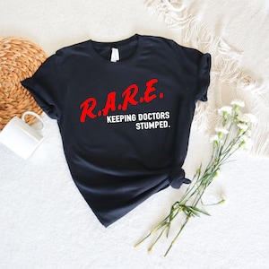 May include: Black t-shirt with the text "R.A.R.E. KEEPING DOCTORS STUMPED." in red lettering.
