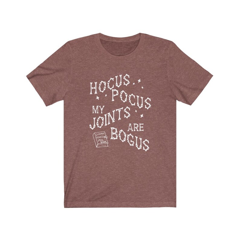 May include: A heather brown t-shirt with a white graphic that reads "Hocus Pocus My Joints Are Bogus" with a small book graphic that says "Chronic Pain Spell Book".
