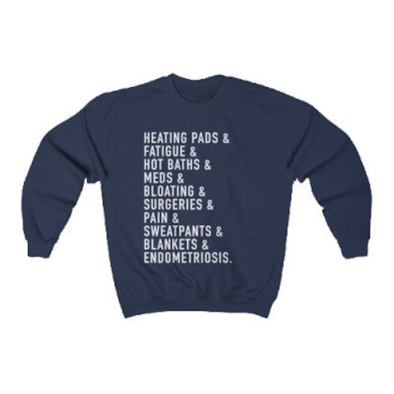 May include: Navy blue sweatshirt with white text that reads "HEATING PADS & FATIGUE & HOT BATHS & MEDS & BLOATING & SURGERIES & PAIN & SWEATPANTS & BLANKETS & ENDOMETRIOSIS."