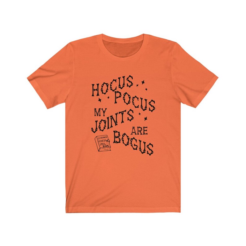 May include: Orange short-sleeved t-shirt with black text that reads "Hocus Pocus My Joints Are Bogus" and a small black and white illustration of a book with the text "Charms,  Finishes,  Spells,  Book".