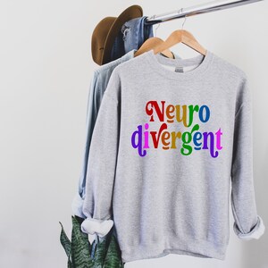 Może przedstawiać: Szara bluza z napisem "Neurodivergentny" w kolorach tęczy.