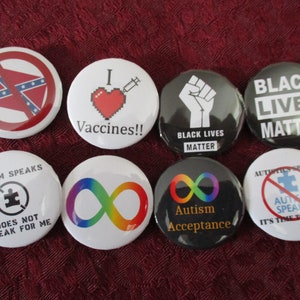 May include: Eight round button pins with various messages and images. The pins include a red, white, and blue pin with a crossed-out Confederate flag, a white pin with a red heart and a syringe, a black pin with a raised fist and the text "Black Lives Matter", a black pin with the text "Black Lives Matter", a white pin with a rainbow infinity symbol, a black pin with a rainbow infinity symbol and the text "Autism Acceptance", a white pin with a black circle and a puzzle piece with the text "Autism Speaks Does Not Speak For Me", and a white pin with a red circle and a crossed-out puzzle piece with the text "Autistics Speak Autism Speak It's Time To Listen".
