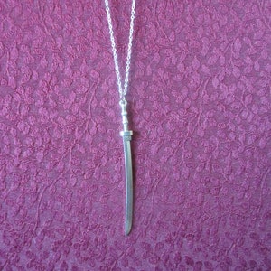 May include: A silver necklace with a silver sword pendant. The sword is about 2 inches long and has a detailed design.