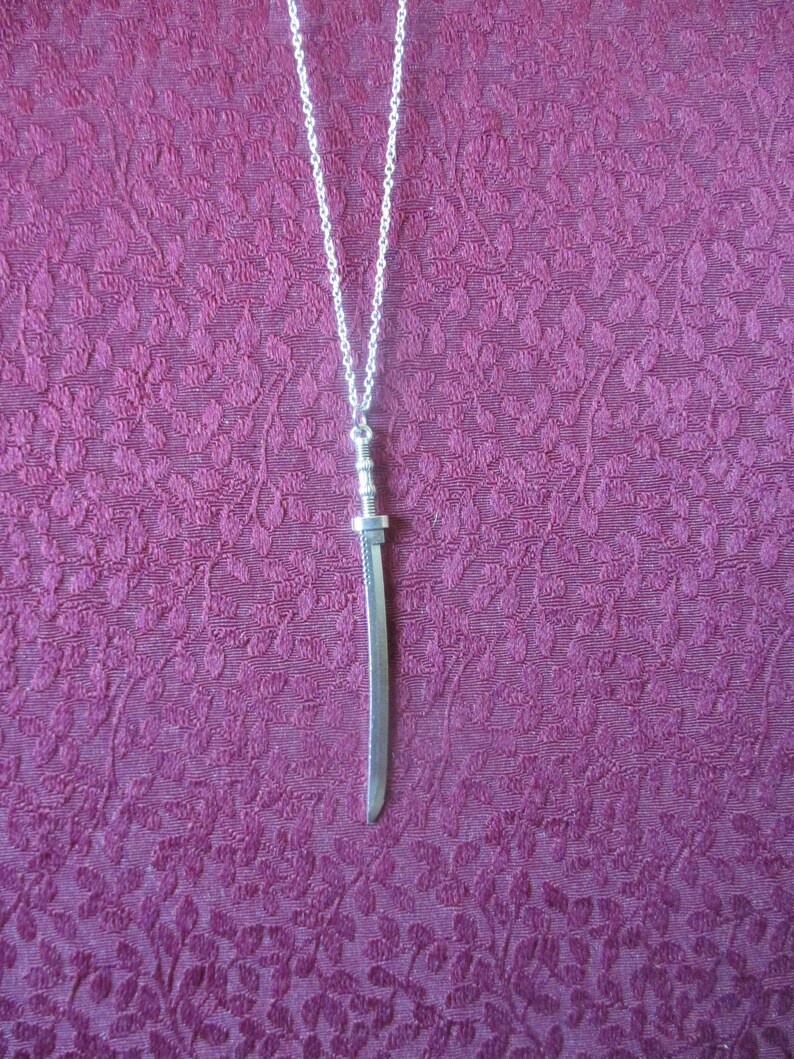 May include: A silver necklace with a silver sword pendant. The sword is about 2 inches long and has a detailed design.
