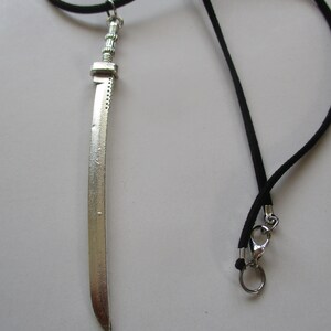 May include: A silver sword pendant on a black cord necklace. The sword has a detailed hilt and a sharp point.