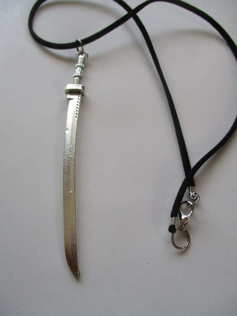 May include: A silver sword pendant on a black cord necklace. The sword has a detailed hilt and a sharp point.