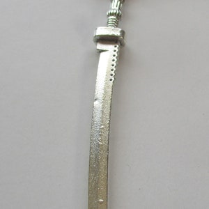 May include: A silver-colored sword pendant necklace with a black cord. The sword has a detailed hilt and a curved blade.