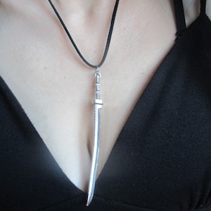May include: A silver sword pendant on a black cord necklace.