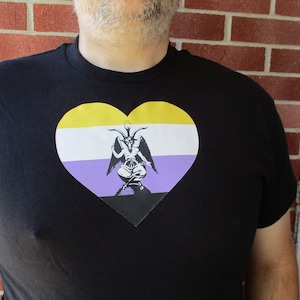 May include: A black t-shirt with a heart-shaped design featuring the colors of the non-binary pride flag and a black and white image of a goat-like figure with wings.