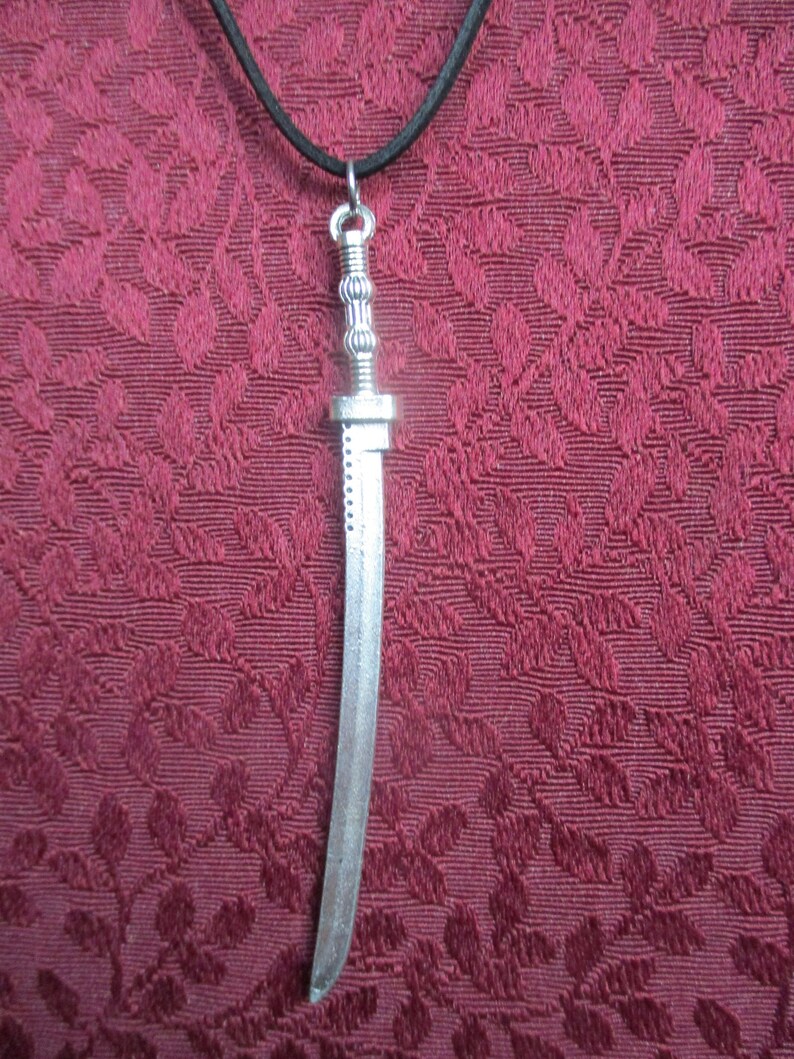 May include: A silver sword pendant on a black cord necklace. The sword has a detailed handle and a curved blade.