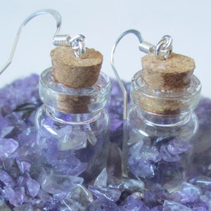 May include: A pair of earrings featuring small glass bottles filled with amethyst chips, each bottle has a cork stopper and a silver hook.