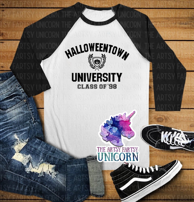 May include: A white and black baseball tee shirt with a black graphic that says "Halloweentown University Class of '98". The graphic includes a crest with a pumpkin inside. The shirt is laying on a wooden surface with a pair of black high-top sneakers and a pair of blue jeans.