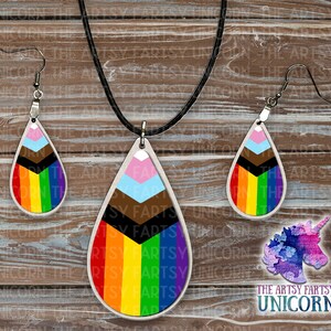 May include: A jewelry set featuring a teardrop pendant necklace and matching earrings. The pendants and earrings display a rainbow flag design with a white border. The set includes a black cord necklace and silver-tone earring hooks. The text "THE ARTSY FARTSY UNICORN" is visible.