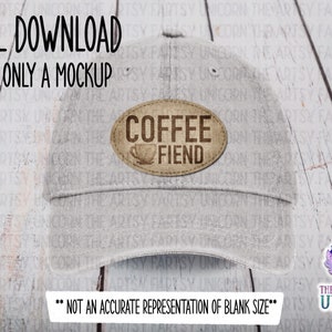 Puede incluir: Una gorra de béisbol gris con un parche ovalado marrón que dice "Coffee Fiend" con un icono de taza de café. El parche tiene un aspecto desgastado. La gorra está sobre un fondo de madera blanca.