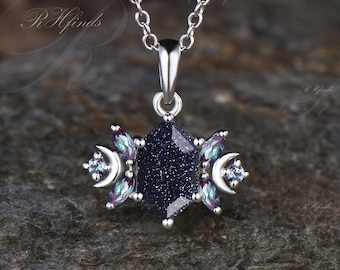 May include: A silver necklace with a blue star-shaped pendant. The pendant is adorned with smaller blue and purple gemstones. The necklace is on a gray textured surface.