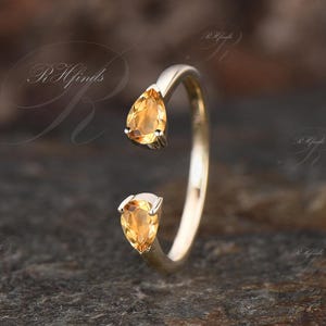 Puede incluir: Un anillo de oro con dos piedras preciosas en forma de lágrima de topacio. El anillo está abierto por un lado y tiene un diseño delicado.