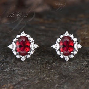 Può includere: Un paio di orecchini d'argento con una pietra ovale rossa circondata da un alone di piccole pietre chiare.