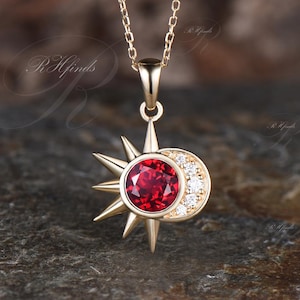 May include: Gold necklace with a red gemstone sun and a crescent moon pendant with clear gemstones.