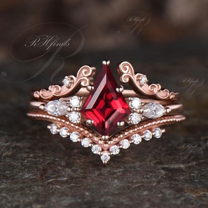 May include: A rose gold engagement ring set with a red gemstone and a delicate, ornate design. The ring features a large, square-shaped red gemstone surrounded by smaller, round diamonds. The band is adorned with intricate details and a row of smaller diamonds.
