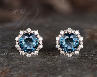 May include: A pair of earrings featuring a round blue gemstone encircled by a halo of smaller white gemstones. The earrings are set in rose gold metal.
