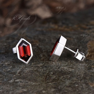 May include: A pair of silver stud earrings with red gemstone accents. The gemstones are set in a geometric shape.