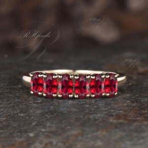 May include: A gold band ring with seven oval-shaped red gemstones set in a row.