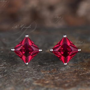 Pode incluir: Um par de brincos de prata com pedras preciosas vermelhas quadradas.