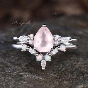 May include: A pear-shaped rose quartz engagement ring set with a delicate band of white opal and diamond accents.