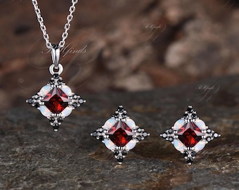 May include: A silver necklace and earrings set featuring a red gemstone surrounded by white opals and black cubic zirconia stones.
