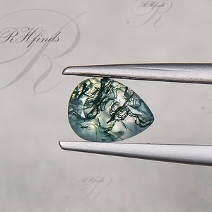 May include: A teardrop-shaped green moss agate gemstone with white and black dendritic patterns, held by tweezers.
