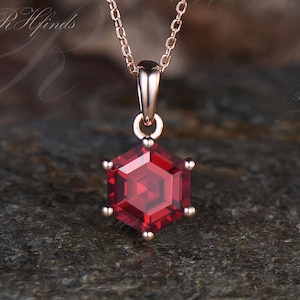 Könnte beinhalten: Eine Halskette aus Roségold mit einem sechseckigen Anhänger, der mit einem roten Edelstein besetzt ist.