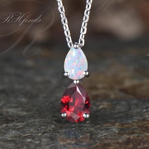 May include: A silver chain necklace with a teardrop-shaped opal gemstone and a teardrop-shaped red gemstone pendant.