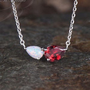 May include: A silver chain necklace with a white opal and a red gemstone pendant. The pendant is shaped like two teardrops.