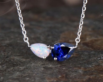 May include: A silver chain necklace with a teardrop-shaped opal and a teardrop-shaped blue sapphire pendant.