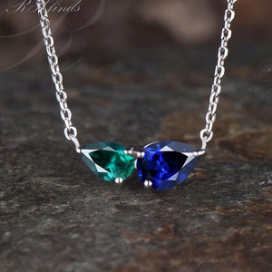 May include: A silver chain necklace with a teardrop-shaped blue gemstone and a teardrop-shaped green gemstone pendant.