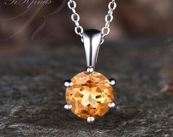 Puede incluir: Un collar de cadena de plata con un colgante redondo de piedra preciosa naranja.