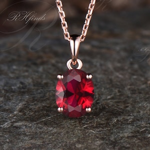 Puede incluir: Un delicado collar de cadena de oro rosa con un colgante que presenta una gran piedra roja de forma ovalada.