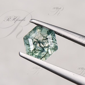 May include: A green moss agate gemstone with a square shape and a unique dendritic pattern. The gemstone is held by tweezers.