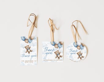 May include: Three baby shower thank you tags with a teddy bear holding balloons. The tags have the words "Thank you" and "For showering us with love" in blue script. The tags are rectangular and circular.