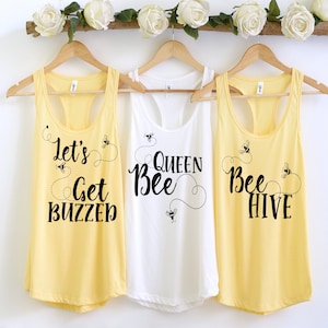 May include: Three yellow tank tops with black text and bee graphics. The tank tops read "Let's Get Buzzed", "Queen Bee", and "Bee Hive".