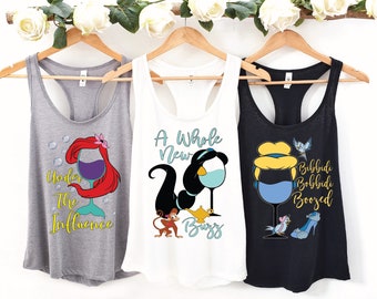 Op de afbeelding: Drie tanktops met een Disney-prinsessen thema. De eerste tanktop is grijs met een zeemeermin die een glas wijn vasthoudt en de tekst "Under the Influence". De tweede tanktop is wit met Jasmine die een glas wijn vasthoudt en de tekst "A Whole New Buzz". De derde tanktop is zwart met Assepoester die een glas wijn vasthoudt en de tekst "Bibbidi Bobbidi Boozed".