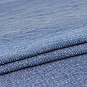 Puede incluir: Primer plano de una tela vaquera azul con un sutil patr&oacute;n texturizado. La tela est&aacute; doblada por la mitad, mostrando el tejido y la textura.