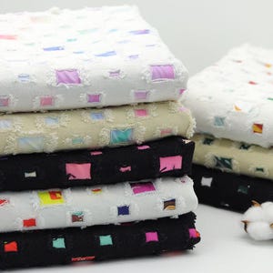 Pode incluir: Uma pilha de tecido de algodão branco com um padrão quadrado. O tecido tem uma borda desfiada e está em camadas de diferentes cores, incluindo preto, bege e branco.