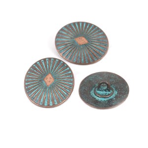 Puede incluir: Tres botones redondos de color cobre con un acabado azul turquesa. Los botones tienen una forma de diamante en relieve en el centro y un diseño de rayos de sol alrededor del diamante. Un botón tiene un bucle en la parte posterior.