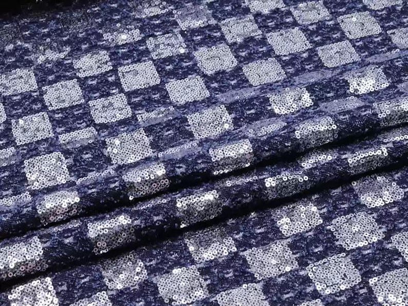 May include: A navy blue fabric with a checkered pattern made of silver sequins.