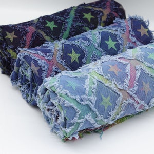 May include: Three rolled up fabric swatches with a star pattern. The fabric is a blue denim with a frayed edge. The stars are green and the background is a mix of blue, green, and pink.