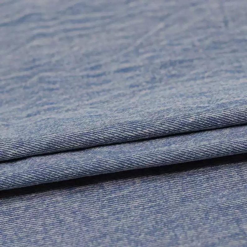 Puede incluir: Primer plano de una tela vaquera azul con un tejido texturizado. La tela est&aacute; doblada sobre s&iacute; misma, mostrando el rev&eacute;s del material.